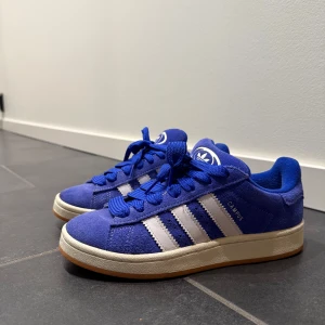 Blå Adidas Campus sneakers  - Snygga blå Adidas Campus sneakers med vita ränder och snörning. Endast använda ett fåtal gånger!
