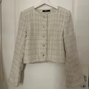 Beige kavaj  - Snygg vit cardigan från gina tricot i ett tweed-liknande material. Kavajen har en croppad passform med knappar framtill och långa ärmar. Perfekt för en stilren look.