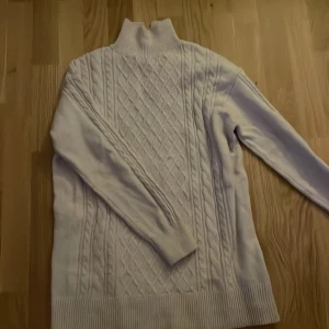 Vit stickad polotröja i längre modell från H&M - Mysig vit stickad polotröja från H&M i storlek S. Tröjan har ett snyggt flätmönster på framsidan och ribbade kanter vid ärmslut och nederkant. Perfekt för kalla höst- och vinterdagar. Håll dig varm och stilren! ❄️