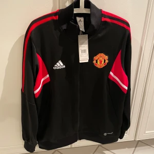 Svart Man United träningsjacka och byxor - Säljer en snygg svart träningsjacka från Adidas med Manchester United-logga. Pris kan diskuteras. Men jag säljer tröjan för 500kr och byxorna för 200kr
