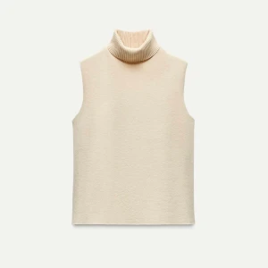 Beige ärmlös polotröja - Säljer en stilren beige ärmlös polotröja. Perfekt för lager-på-lager under höst och vår. Den har en mjuk och bekväm passform med en hög polokrage som ger en elegant touch. Passar både till vardags och lite finare tillfällen.