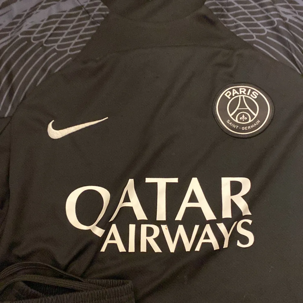 Säljer en snygg svart PSG fotbollströja från Nike. Den har korta ärmar och ett stilrent märke på bröstet. Perfekt för alla fotbollsfans som vill visa sitt stöd för Paris Saint-Germain. Tröjan har också Qatar Airways som sponsorlogga. Passar perfekt till både träning och vardag!. T-shirts.