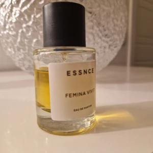 Essnce Femina Vivit Eau de Parfum - Säljer en elegant flaska Essnce Femina Vivit Eau de Parfum. Den har en stilren design med en genomskinlig glasflaska och svart kork. Perfekt för den som vill ha en sofistikerad doft i sin samling.