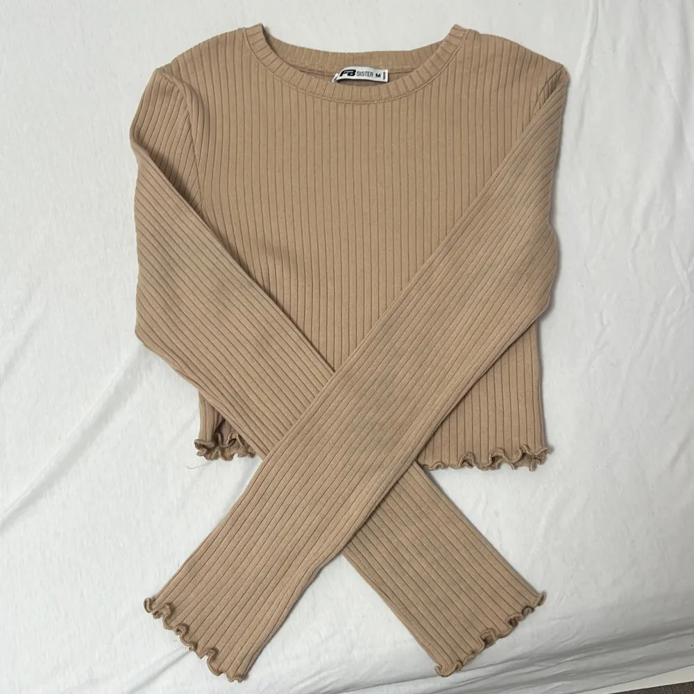 Säljer en superfin beige ribbad tröja från FB Sister i storlek M. Den är croppad med långa ärmar och har en söt volangdetalj vid nederkanten. Perfekt för både höst och vår! 🧡. Neuletakit & Villapaidat.