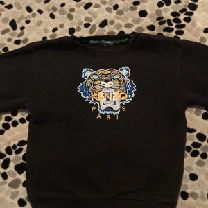 Svart Kenzo tröja med tigerbroderi - Säljer en svart Kenzo tröja med ett coolt tigerbroderi på framsidan. Tröjan har långa ärmar och är i mycket bra skick. Perfekt för höst och vinter, och den är superbekväm att ha på sig. Passar både till vardags och festliga tillfällen!