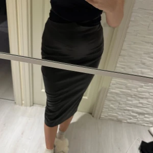Svart kjol - Snygg svart kjol i tight passform. Perfekt för både vardag och fest! Kjolen är knälång och har en stilren design som passar till det mesta. Materialet ser ut att vara mjukt och stretchigt, vilket gör den bekväm att bära hela dagen. Passar s/m/l storlek 