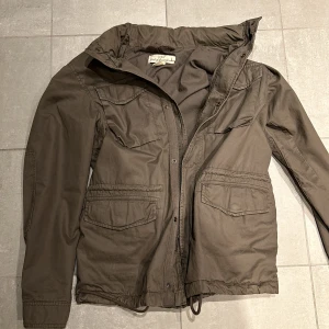 Field Jacka - Tja! Säljer nu denna Field Jackan från Logg. Den är i typ en grå/khaki färg och passar S. Den har snören nertill så man kan tajta upp den så den sitter bättre. Hör av vid Frågor!