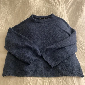 Mörkblå stickad tröja - Mysig mörkblå stickad tröja med rund hals och långa ärmar. Perfekt för kyliga dagar och ger en avslappnad look. Ribbstickade kanter vid ärmslut och nederkant.