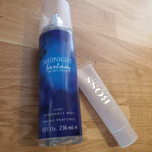 Bodyspray+Bodylotion 236ml - Body spray Midnight Fantasy av Britney Spears i en blå sprayflaska på 236 ml, perfekt för en mystisk och fruktig doft. Oöppnad Bodylotion Boss The Scent 50ml i en elegant beige tub, idealisk för en sofistikerad och sensuell doftupplevelse. 