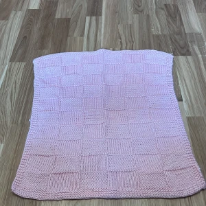 Rosa stickad filt - Mysig rosa stickad filt med rutmönster. Perfekt för att hålla sig varm under kyliga kvällar. Den har en mjuk och bekväm känsla.