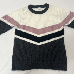 Randig stickad tröja i flera färger - Säljer en superfin stickad tröja med randigt mönster i vitt, rosa och svart. Tröjan har en bekväm passform och långa ärmar, perfekt för höst och vinter. Den är ribbad och känns riktigt mysig. Perfekt för att hålla sig varm och stilren under kyliga dagar!. Tröjan är använd en gång. Denna tröjan är barn som är 10-12 år. Köp på Lindex :) Priset kan diskuteras. 