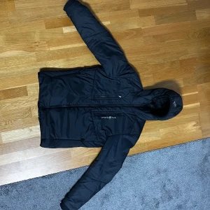 Svart jacka från Sail Racing - Säljer en svart jacka från Sail Racing i mycket bra skick. Den är perfekt för höst och vinter med sitt varma material och stilrena design. Jackan har en dragkedja framtill och en praktisk huva. Perfekt för dig som vill hålla stilen även när det är kallt ute! Köpt för 2400kr nypris säljer beroende av felköp,!