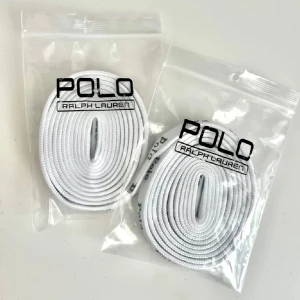 Vita skosnören från Ralph Lauren - Två par vita skosnören från Ralph Lauren, förpackade i plastpåsar. Skosnörena har texten 'Polo' tryckt längs sidorna och är perfekta för att ge dina skor en stilren look.