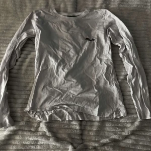 Vit långärmad tröja från Fila - Säljer en vit långärmad tröja från Fila. Perfekt för en avslappnad stil med sin enkla design och bekväma passform. Tröjan har en rund halsringning och Fila-loggan på bröstet. Passar bra till både jeans och mjukisbyxor. ⚠️ni betalar för frakten⚠️