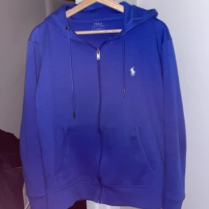 Blå hoodie från Polo Ralph Lauren - Säljer en snygg blå hoodie från Polo Ralph Lauren i storlek S. Den har en dragkedja framtill och en klassisk logga på bröstet. Perfekt för både vardag och chill. Den är i bra skick och superbekväm att ha på sig. Passar perfekt till höst och vår!