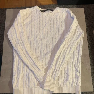 Fin stickad tröja från pullover Factory, jätte skön ha på sig under vinter, färgen är vit och storleken är S  - Säljer en superfin vit stickad tröja från Pullover Factory. Den har ett klassiskt flätmönster och är perfekt för både höst och vinter. Tröjan är långärmad och har ribbade muddar vid ärmslut och nederkant. Perfekt för att hålla sig varm och stilren! Storleken är S och färgen är vit, kom med frågor med mera