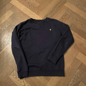 Svart sweatshirt med gul logga från Lyle scott  - Säljer en stilren svart sweatshirt med en liten gul logga på bröstet. Tröjan har långa ärmar och är perfekt för både vardag och avslappnade tillfällen. Den är i bra skick och passar perfekt till jeans eller chinos.  Pris kan diskuteras. 