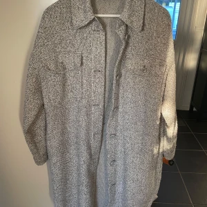 Grå overshirt från Vero Moda - Säljer en snygg grå overshirt från Vero Moda i storlek M. Den har en avslappnad passform med långa ärmar och knappar framtill. Perfekt för höst och vår, och funkar både som jacka och skjorta. Materialet är mjukt och bekvämt, vilket gör den idealisk för lager-på-lager-stil.