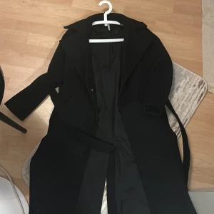 Svart kappa - Elegant svart kappa med klassisk design. Den har långa ärmar och en stilren krage. Perfekt för kyligare dagar och ger en sofistikerad look.