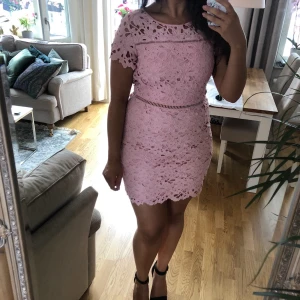 Rosa spetsklänning med öppen rygg - Säljer en superfin rosa spetsklänning med korta ärmar och öppen rygg. Perfekt för sommarens fester! Klänningen har ett vackert blommigt mönster och en tight passform som framhäver figuren. Den är i mycket bra skick och redo för nya äventyr. 🌸