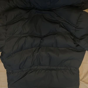 Svart dunjacka från Boomerang - Säljer en klassisk svart dunjacka från Boomerang i storlek XS. Jackan är perfekt för kalla vinterdagar med sin tjocka vaddering och långa ärmar. Den har både dragkedja och knappar. Använd endast i en månad. 