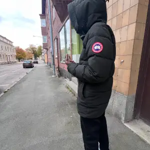 Säljer en svart dunjacka från Canada Goose i mycket bra skick. Jackan är perfekt för vintern med sin varma och vadderade design. Den har en huva och dragkedja framtill. Passar perfekt för kalla dagar och har en klassisk stil.