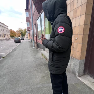 Svart dunjacka från Canada Goose  - Säljer en svart dunjacka från Canada Goose i mycket bra skick. Jackan är perfekt för vintern med sin varma och vadderade design. Den har en huva och dragkedja framtill. Passar perfekt för kalla dagar och har en klassisk stil.