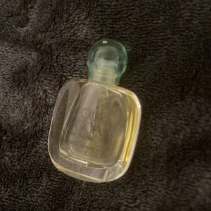 Parfymflaska med grön kork - Säljer en elegant parfymflaska med en unik form och en grön kork. Flaskan är genomskinlig och innehåller en ljusgul doft. Perfekt för att ge en touch av lyx till din samling eller som en fin present.