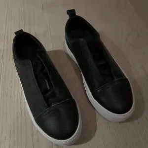 Snygga svarta sneakers i skinn med vit sula från Jim Rickey. De har en stilren design utan snörning, vilket gör dem enkla att ta på och av. Perfekta för en casual look och passar till det mesta i garderoben. Skorna är i nyskick (oanvända) och redo för nya äventyr!