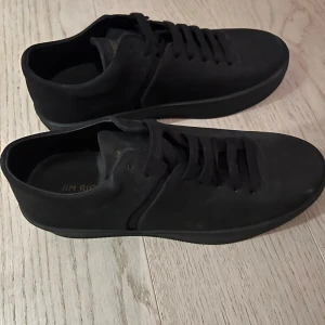 Svarta sneakers från Jim Rickey - Säljer ett par stilrena svarta sneakers från Jim Rickey. De är i nyskick (oanvända) och har en klassisk design med snörning. Perfekta för både vardag och fest. 