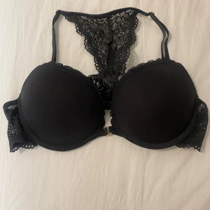 Svart spets-bh - Snygg svart bh med spetsdetaljer och vadderade kupor. Den har en unik design med spets på ryggen och justerbara axelband. Perfekt för att känna sig både bekväm och elegant. Passar till både vardag och speciella tillfällen.