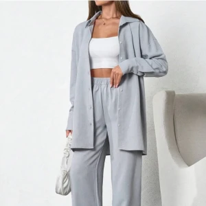 Grå/blå mjukisbyxor med skjorta - Säljer ett set med grå/blåa mjukisbyxor och matchande skjorta. Byxorna har en loose passform med elastisk midja för extra komfort. Skjortan har knappar hela vägen. Dålig på bild, därav bild från hemsidan. Helt oanvänd. 