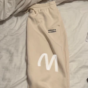 Beige mjukisbyxor från Adidas - Säljer ett par superbekväma beige mjukisbyxor från Adidas. De har en elastisk midja med snörning och en snygg logga på benet. Perfekta för chill dagar hemma eller en avslappnad promenad. 🛋️