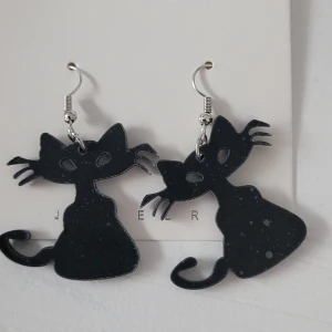  Helt nya Svarta kattformade örhängen - Säljer ett par unika svarta örhängen i form av katter. De är gjorda av ett lätt material och har en stilren design med krokfäste i silverfärg. Perfekta för kattälskare som vill ha något annorlunda i sin smyckessamling!