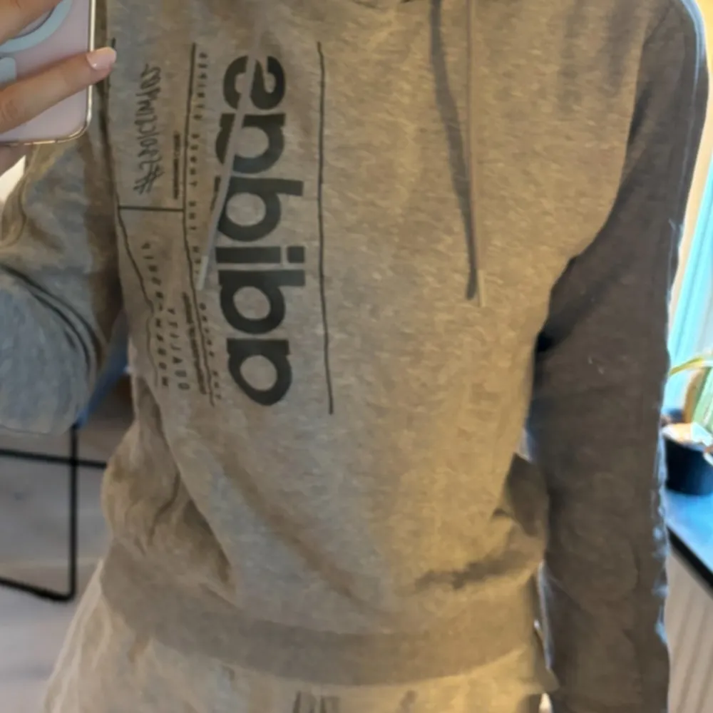 Säljer en snygg och bekväm grå hoodie från Adidas. Den har en stor logga på framsidan. Perfekt för både träning och vardag. Huvan har justerbara snören för bästa passform.. Hoodies.