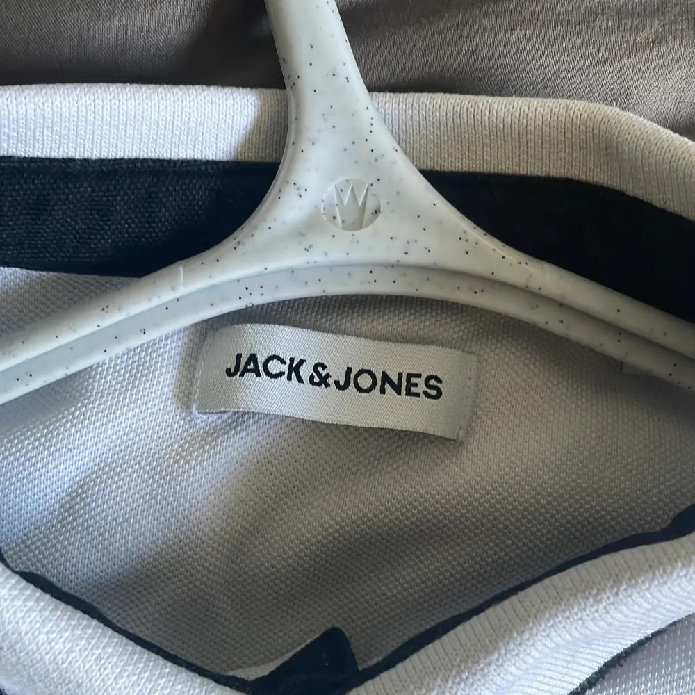 Säljer en stilren vit pikétröja från Jack & Jones. Den har korta ärmar och en klassisk krage med knappar. Tröjan är i bomull och har en liten broderad logga på bröstet.. T-shirts.