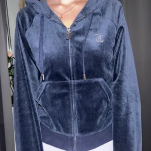 Blå velour hoodie från Juicy Couture - Säljer en supermjuk och snygg blå velour hoodie från Juicy Couture. Den har en dragkedja framtill och en stor luva. På baksidan finns det ikoniska 'Juicy' i glittriga stenar. Perfekt för en chill dag eller när du vill känna dig extra glamorös. 🦋