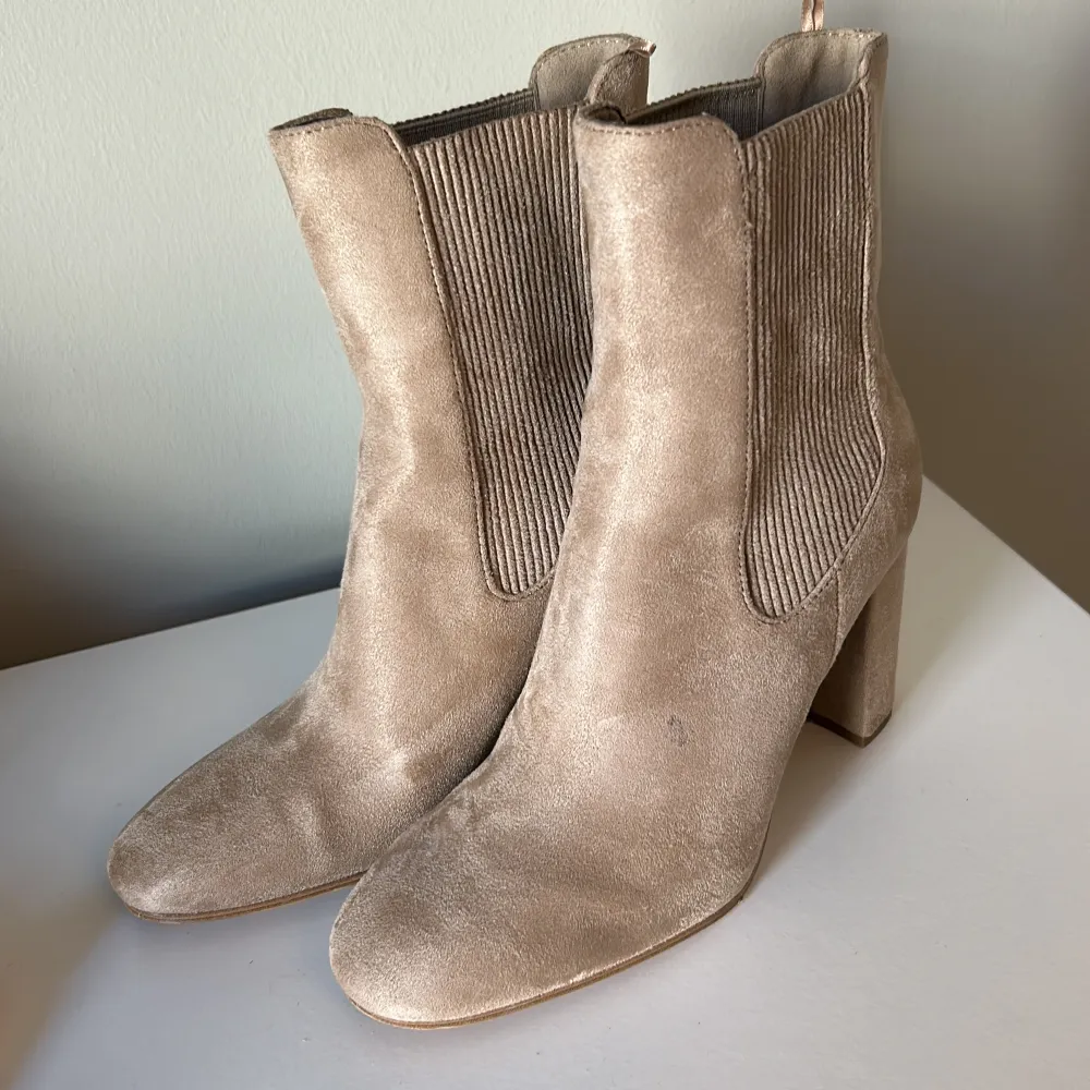 Säljer ett par snygga beige stövletter i mocka. De har en stilren design med en bekväm klack och elastiska paneler på sidorna för enkel på- och avtagning. Perfekta för både vardag och fest!. Kengät.
