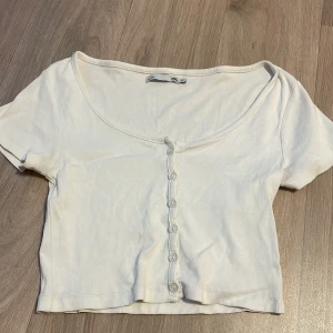 Vit ribbad topp med knappar - Säljer en söt vit ribbad topp med korta ärmar och knappar framtill. Perfekt för sommardagar eller som ett basplagg i garderoben. Toppen har en croppad passform och är superbekväm att bära.