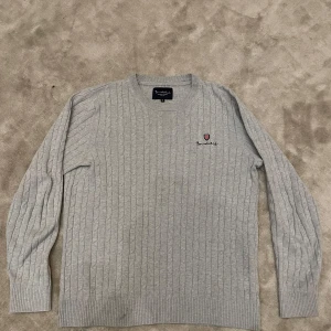 kabel stickad tröja  - Säljer en stilren grå stickad tröja från Bondelid med ett diskret broderat emblem på bröstet. Tröjan har ett klassiskt kabelstickat mönster och långa ärmar, perfekt för kyligare dagar. Tröjan är i nytt skick och har bara testat på 1 gång. Priset är inte spikat i sten👍! Hör av vid minsta lilla fundering🤗