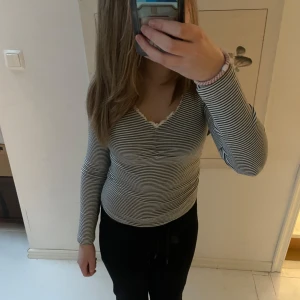 Randig långärmad topp från Holly & Whyte - Säljer en randig långärmad topp från Holly & Whyte by Lindex. Toppen har en v-ringad design med små volangdetaljer vid halsen. 