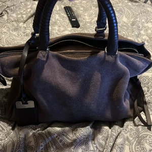 Brun mockaväska med svarta detaljer från Zara - Snygg brun mockaväska från Zara med svarta handtag och detaljer. Väskan har en praktisk dragkedja och en yttre ficka för extra förvaring. Perfekt för dig som vill ha en stilren och funktionell väska. På sista bilden visar jag dragkedjan som går att stänga men notera att flerpen eller den delen man stänger väskan med inte sitter kvar😊Men väskan går fortfarande att stänga fint😇Innuti väskan har tyget gått upp vilket uppfattas som ett stort hål men kan skicka bild privat om man vill de🥰 