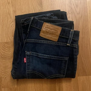 Mörkblå jeans från Levi's 512 - Snygga mörkblå jeans från Levi's med klassisk femficksdesign och en läderpatch på baksidan. Jeansen har en rak passform och är perfekta för en avslappnad stil. De har en knappgylf och är tillverkade i slitstarkt denim.                                           Storlek:                                                                              W:30 L:32