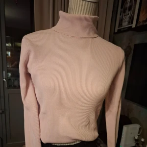 Ljusrosa ribbad polotröja från City Silk - Säljer en stilren ljusrosa polotröja från City Silk. Tröjan är ribbad och har en hög krage som ger en elegant look. Materialet består av en blandning av silke, viskos och nylon vilket gör den mjuk och stretchig. Perfekt för kyligare dagar.