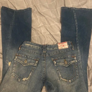 True Religion - Snygga blå bootcut jeans från True Religion med slitna detaljer och klassiska bakfickor med knappar. De är i storleken W26 och säljer då dom tyvärr va för små för mej. Perfekta för en avslappnad stil med en touch av vintage. Jag är 171 cm och dom är i perfekt längd för mej!
