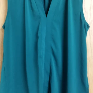 Grön ärmlös topp - Säljer en stilren grön ärmlös topp i mjukt material. Perfekt för varma dagar eller som ett lager under en kavaj. Tillverkad av 93% polyester och 7% elastan för en bekväm passform.