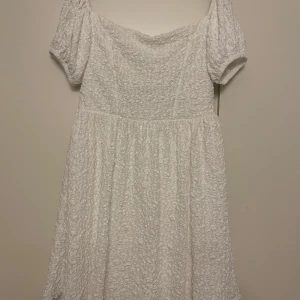 Vit klänning från Gina Tricot - Säljer en söt vit klänning från Gina Tricot med korta puffärmar och en offshoulder-design. Klänningen har en texturerad yta som ger den en unik look. Perfekt för sommarens alla tillfällen!