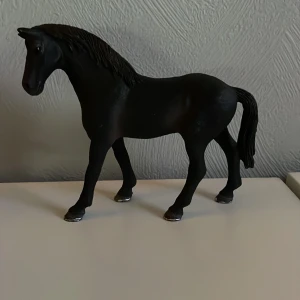 Schleich häst - Säljer en elegant svart hästfigur i plast. Den har en realistisk design med detaljerad man och svans. Perfekt för samlare eller som dekoration i hemmet. 🐴