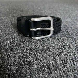 Svart bälte med silverfärgat spänne - Snyggt svart bälte med ett stilrent silverfärgat spänne. Bältet har en flätad design som ger det en unik look. Perfekt för att komplettera din outfit med en touch av stil.