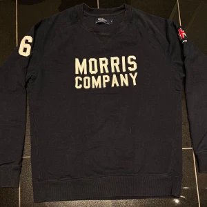Svart sweatshirt från Morris - Säljer en svart sweatshirt från Morris Company med tryck på bröstet och siffran ”68” på ärmen. Tröjan är tillverkad i 100% bomull och har långa ärmar. Perfekt för en avslappnad stil.